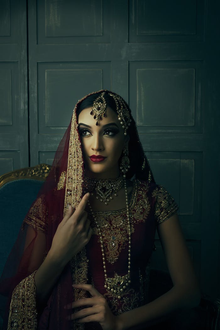Stunning portrait of a woman wearing intricate traditional jewelry and maroon sari, exuding elegance and grace.